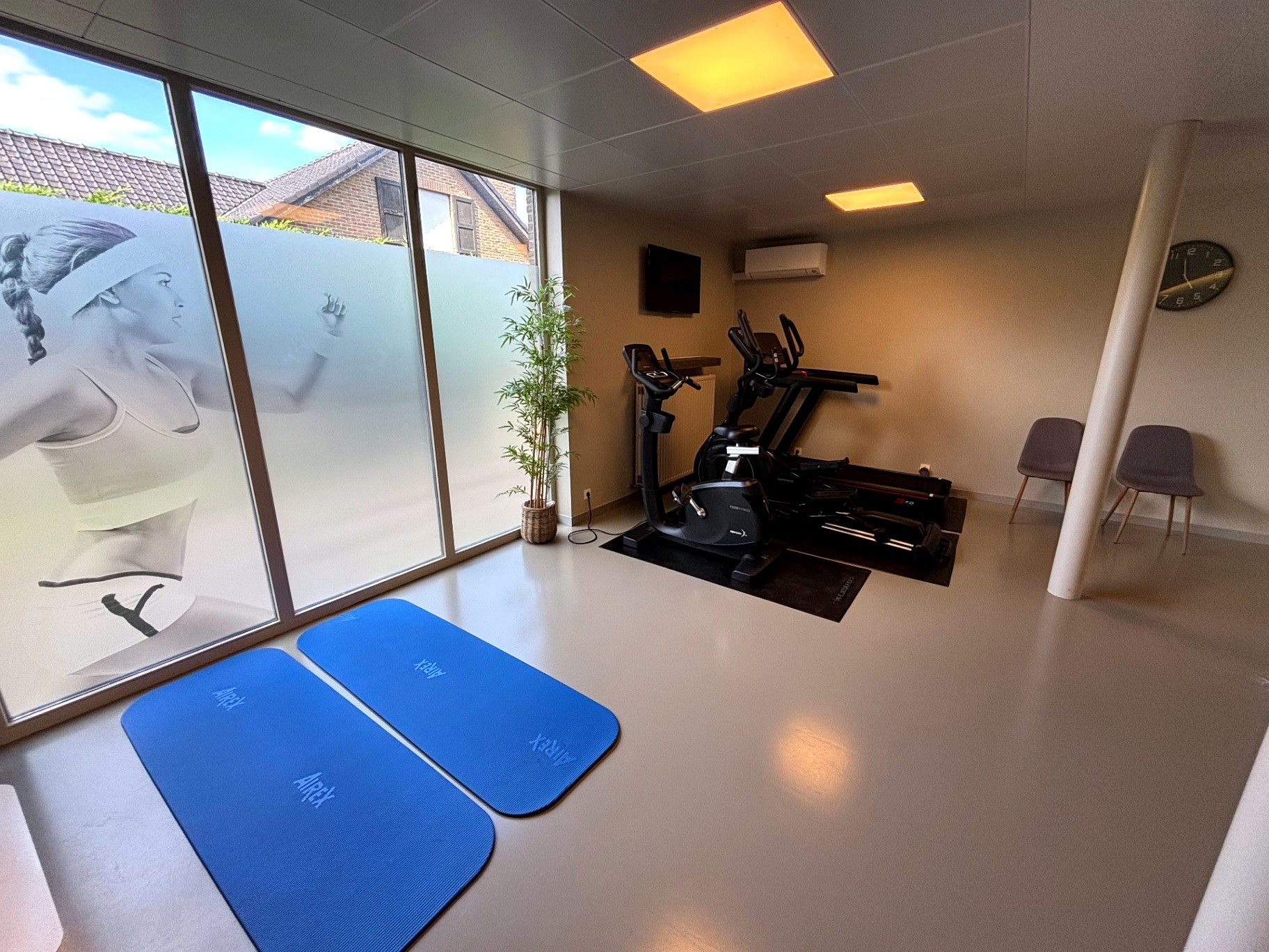 Lichte oefenzaal voor kinesitherapie met matten, cardio en oefenmateriaal in Praktijk West